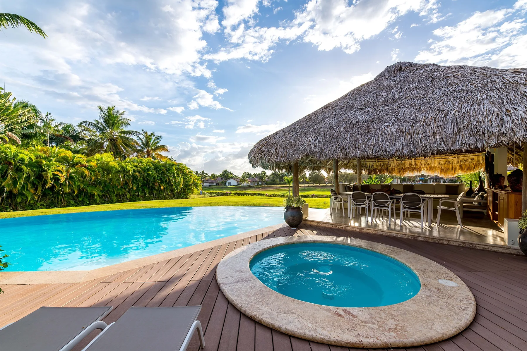 Una piscina al aire libre y un spa redondo están junto a un comedor con techo de paja.