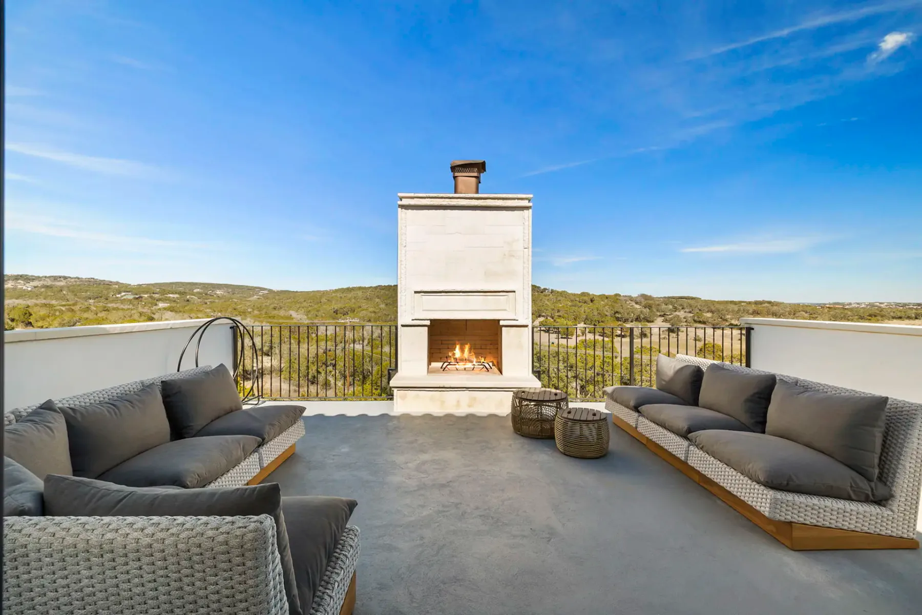 Outdoor terrace with two gray sofas, a central fireplace, and sweeping views of rolling hills under a clear blue sky.