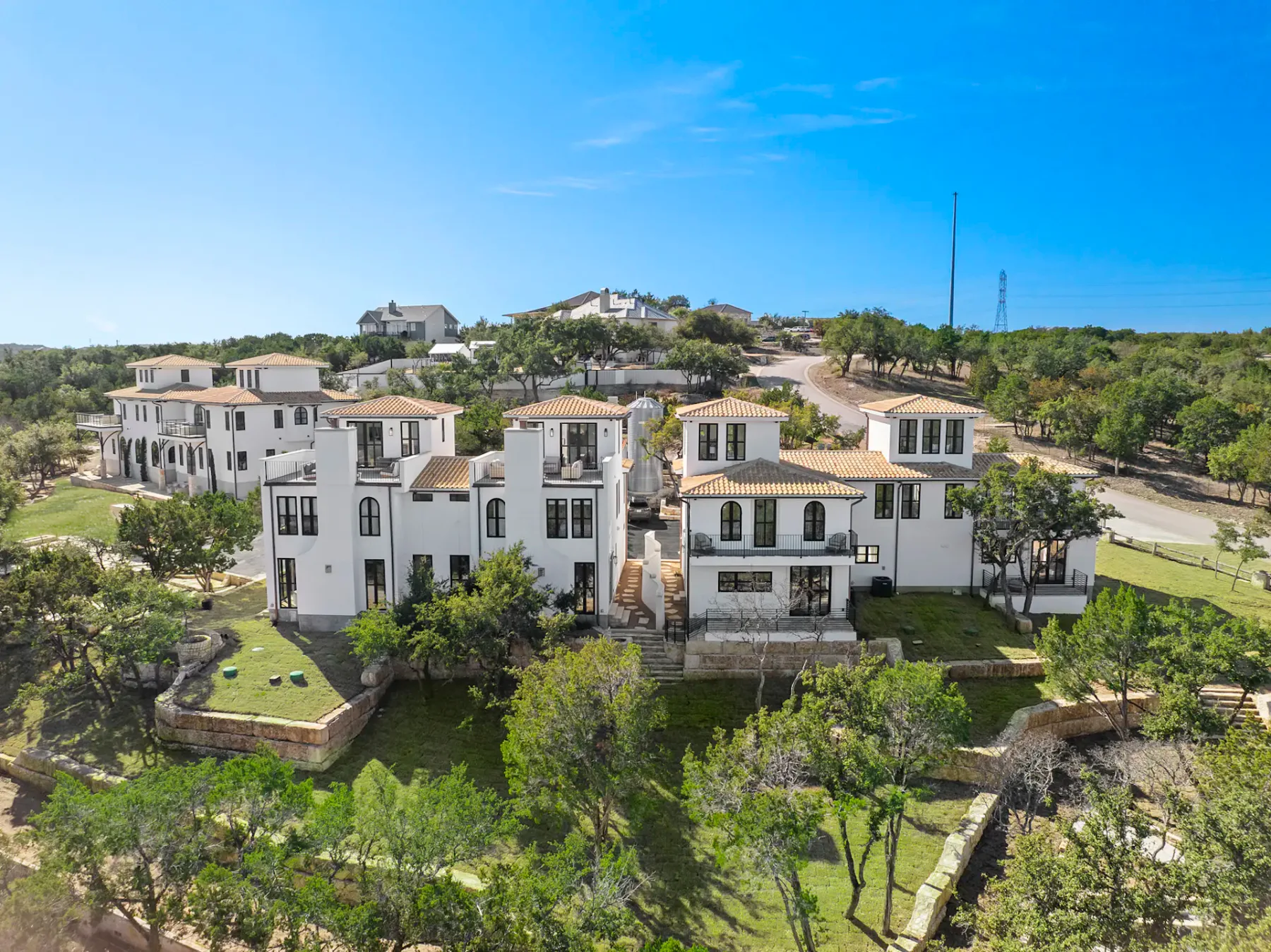 Aerial view of white buildings with tiled roofs among trees and landscaped grounds.