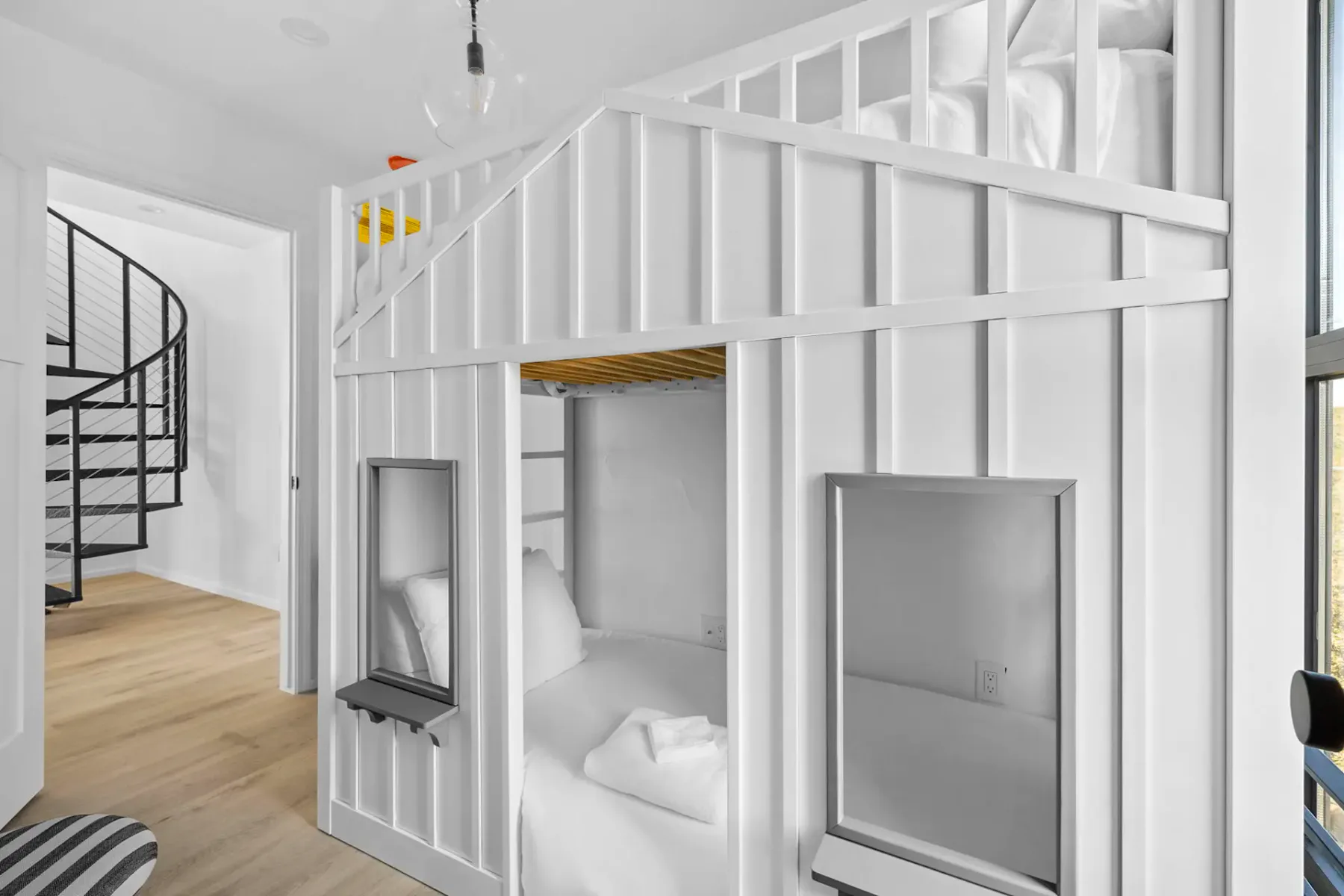 White built-in bunk beds with a small window, beside a spiral staircase.