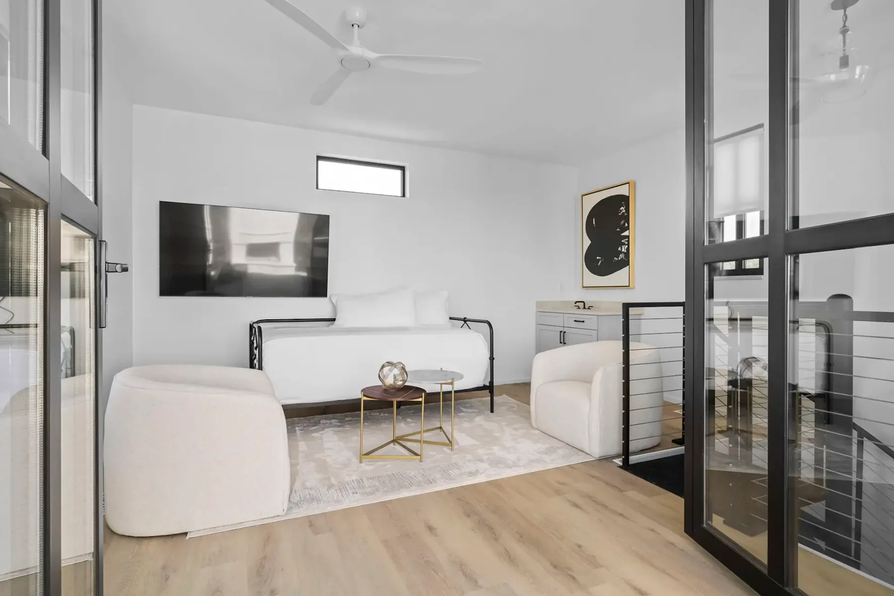 A bright living room with a wall-mounted television, pale seating, and a glass door.
