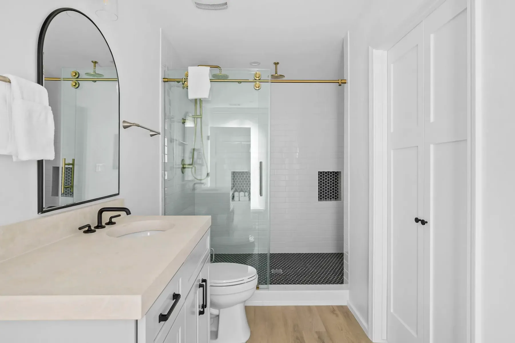 A bright bathroom with a glass shower, white vanity, and light-colored flooring.