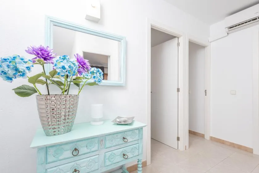 A bright hallway features a turquoise dresser topped with a vase of flowers.