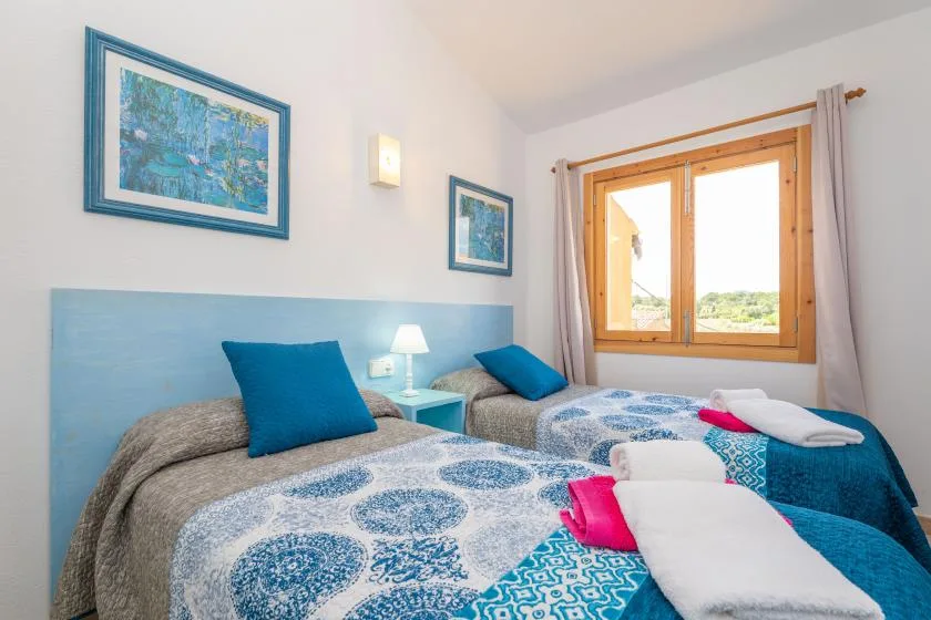 A bright bedroom with two beds, blue patterned bedding, and a window.