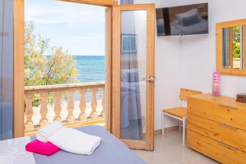 A bedroom opens onto a balcony overlooking the sea, with a bed in the foreground.