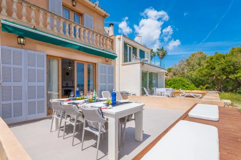 A sunny outdoor dining terrace beside the house, with a table and lounge seating.
