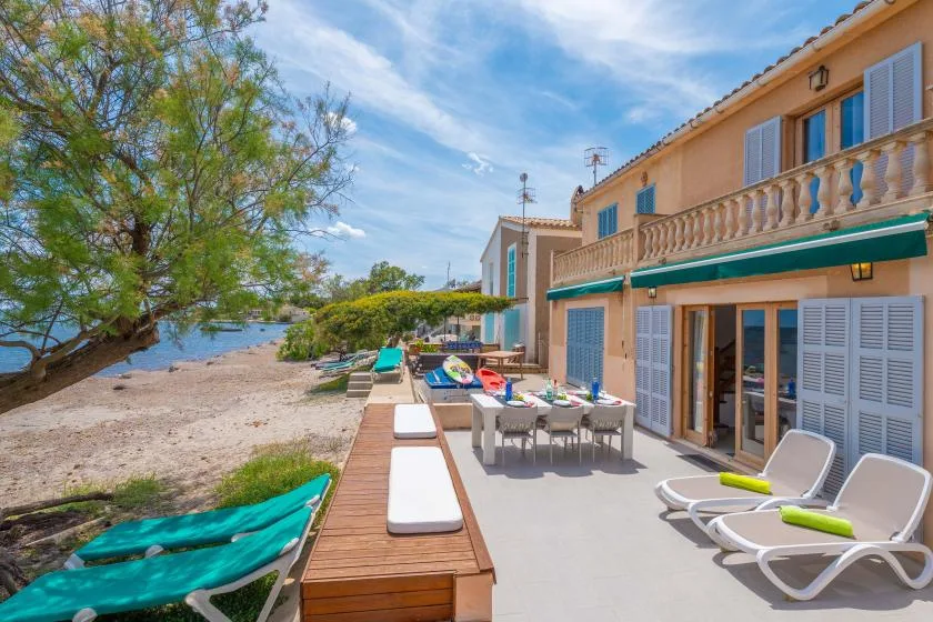 A seaside patio with outdoor seating and lounge chairs beside a small beach.