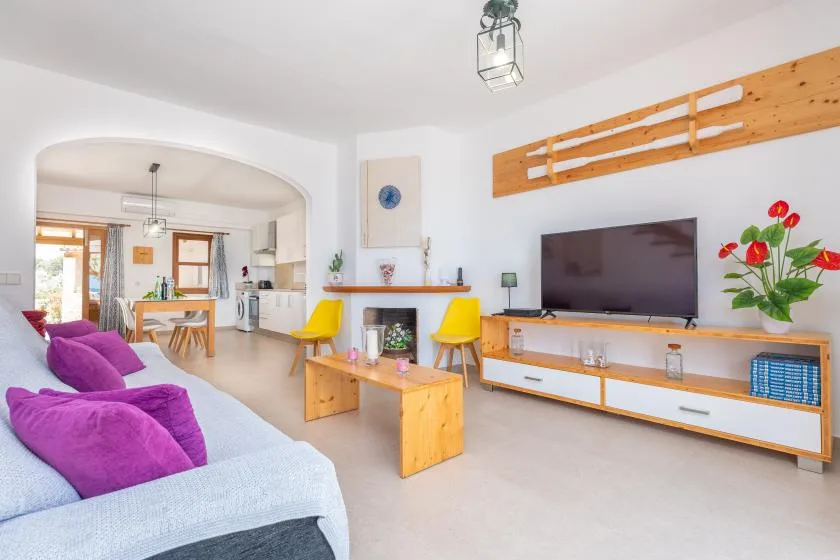 A bright living room with seating, a television, and a dining area in the background.