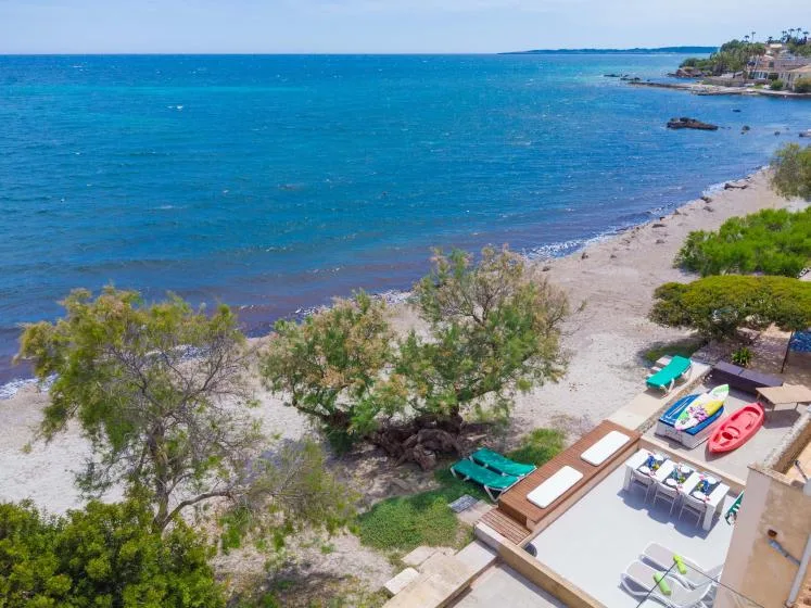 A seaside beach with turquoise water, trees, and a small outdoor seating area.