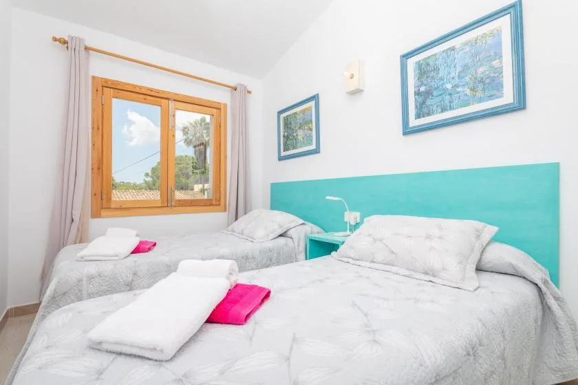 A bright bedroom with two beds and a window overlooking greenery.