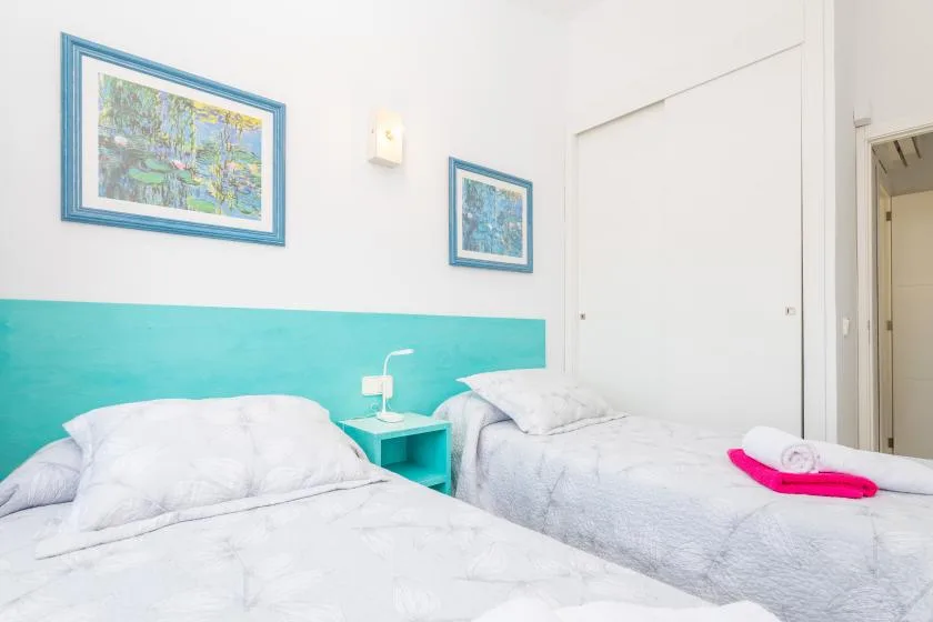 A bright bedroom with two beds and framed artwork on the walls.