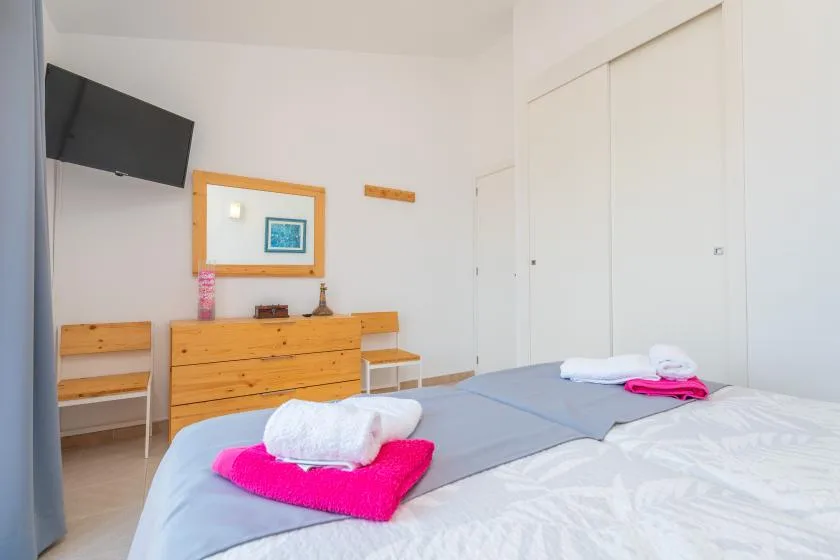 A bright bedroom with beds, wooden drawers, and a wall-mounted television.