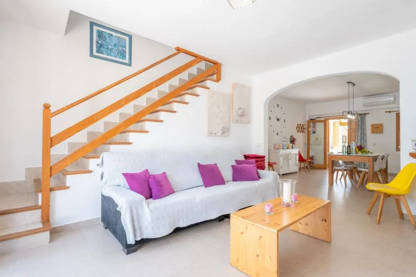 A bright living room with a sofa beneath an open staircase and a dining area beyond.