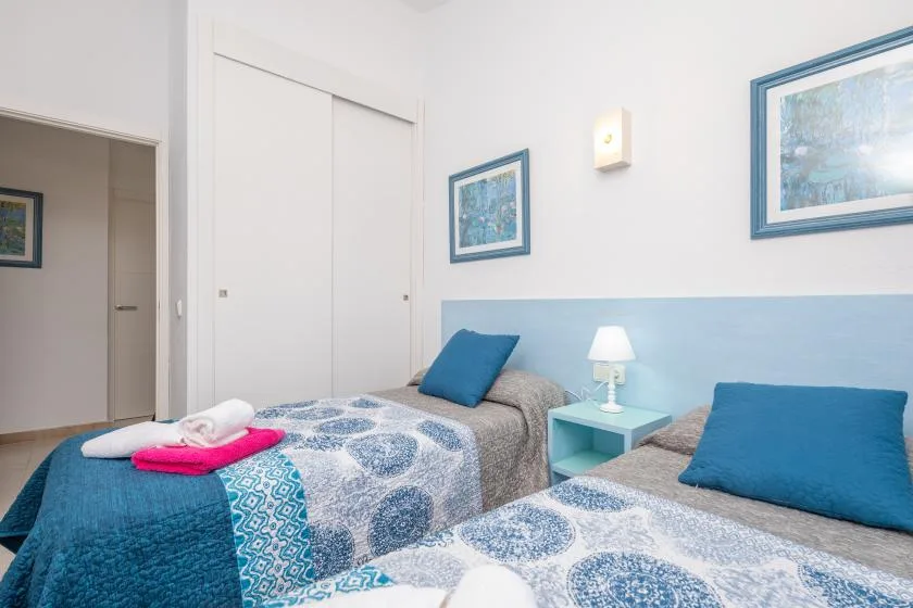 A bedroom with two beds, blue bedding, and framed pictures on the walls.