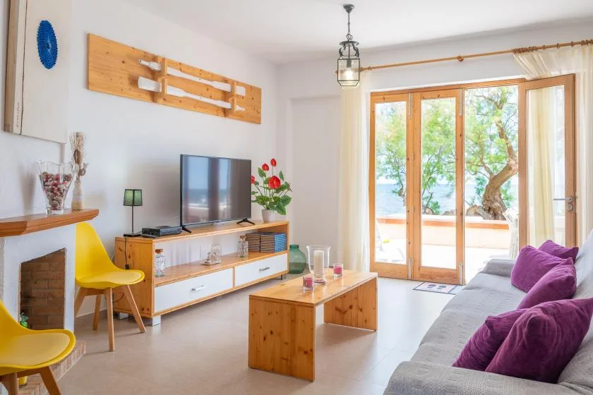 A bright living room with seating, a television, and glass doors opening onto a leafy view.