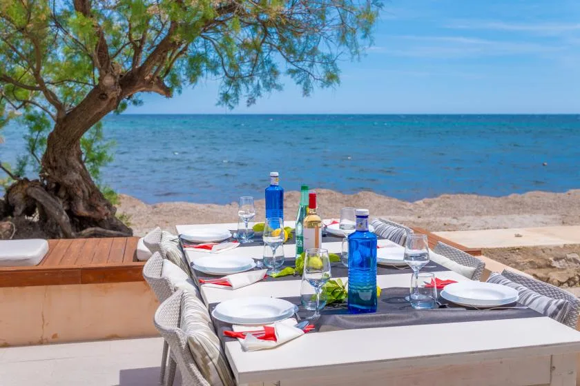 An outdoor dining table is set beside the beach, with the sea in the background.