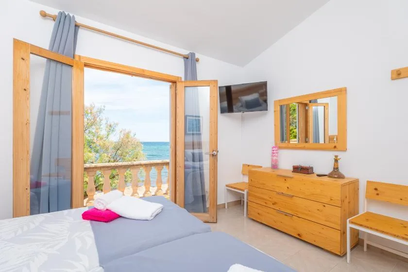 A bedroom with a bed, wooden dresser, and open doors overlooking the sea.