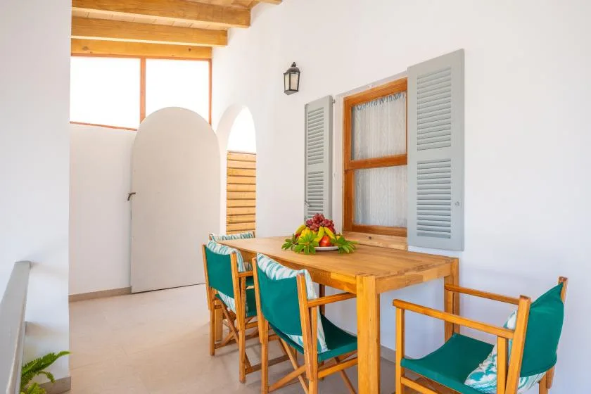 A wooden dining table with teal seating sits beneath a window in a bright room.
