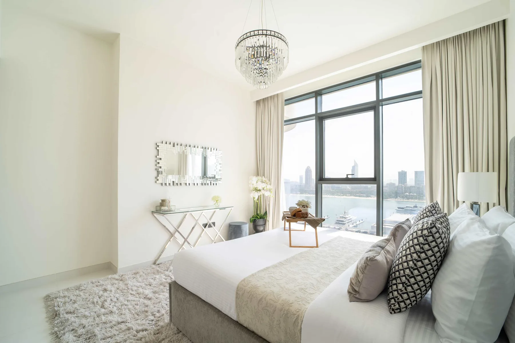 Dormitorio luminoso con una cama grande junto a ventanales con vistas a la ciudad.
