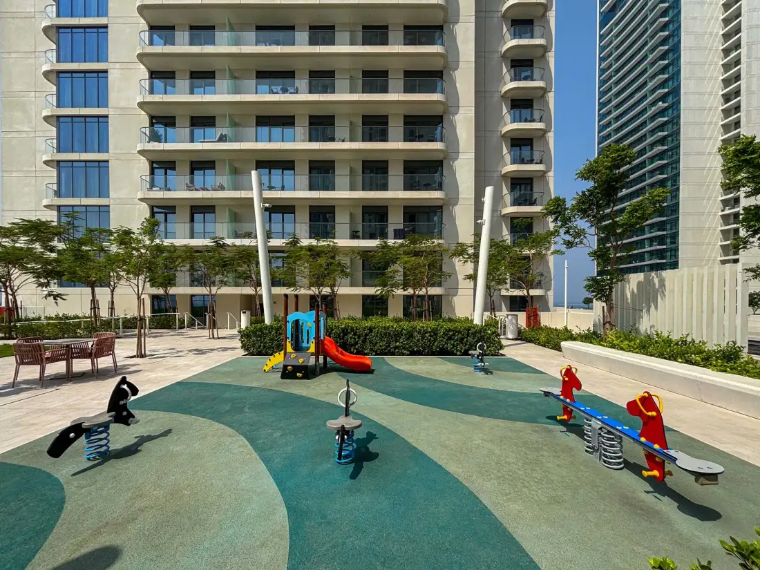 Un parque infantil con juegos de resorte de colores está entre edificios residenciales altos.