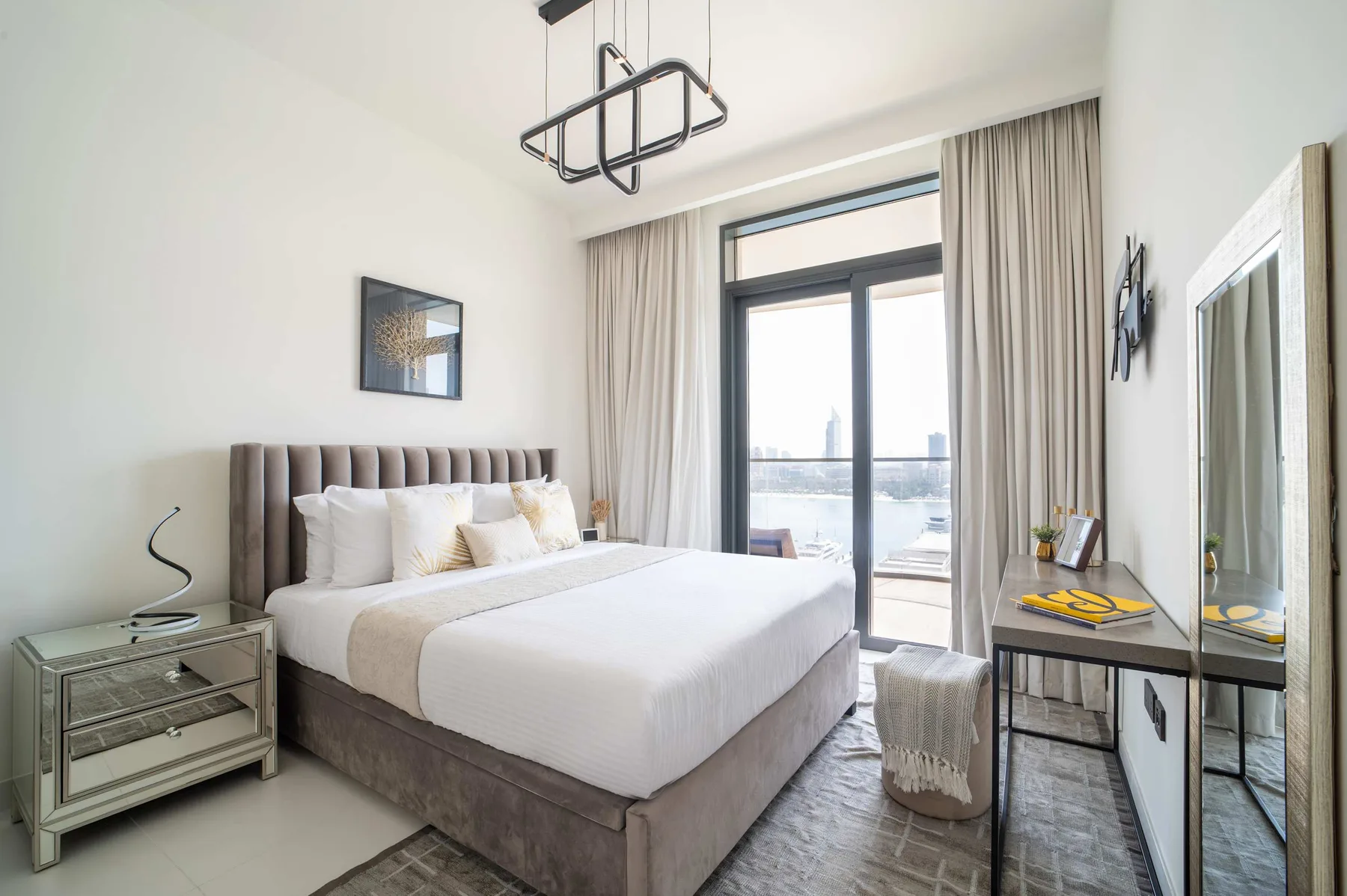 Un dormitorio luminoso con una cama grande junto a puertas de vidrio y cortinas largas.