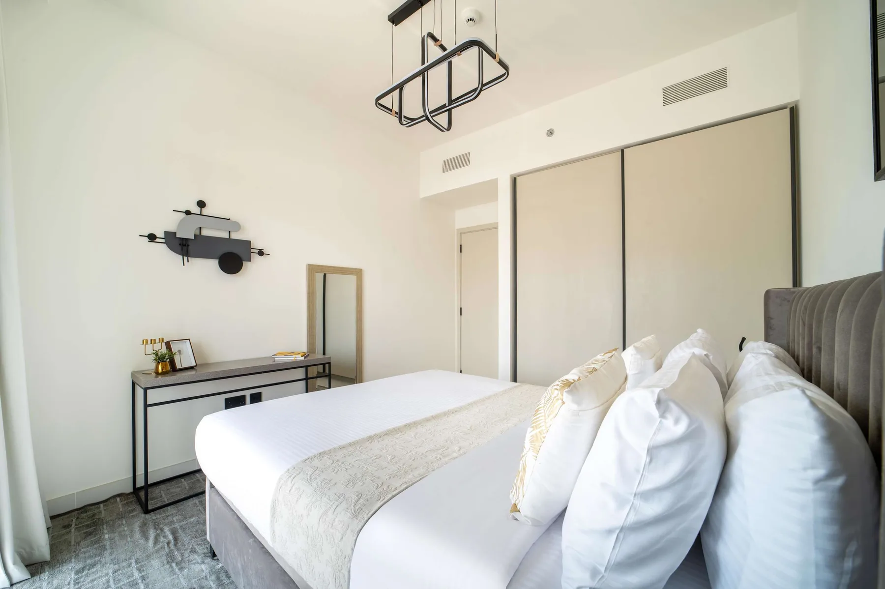 Un dormitorio luminoso con una cama bien hecha y un escritorio junto a la pared.