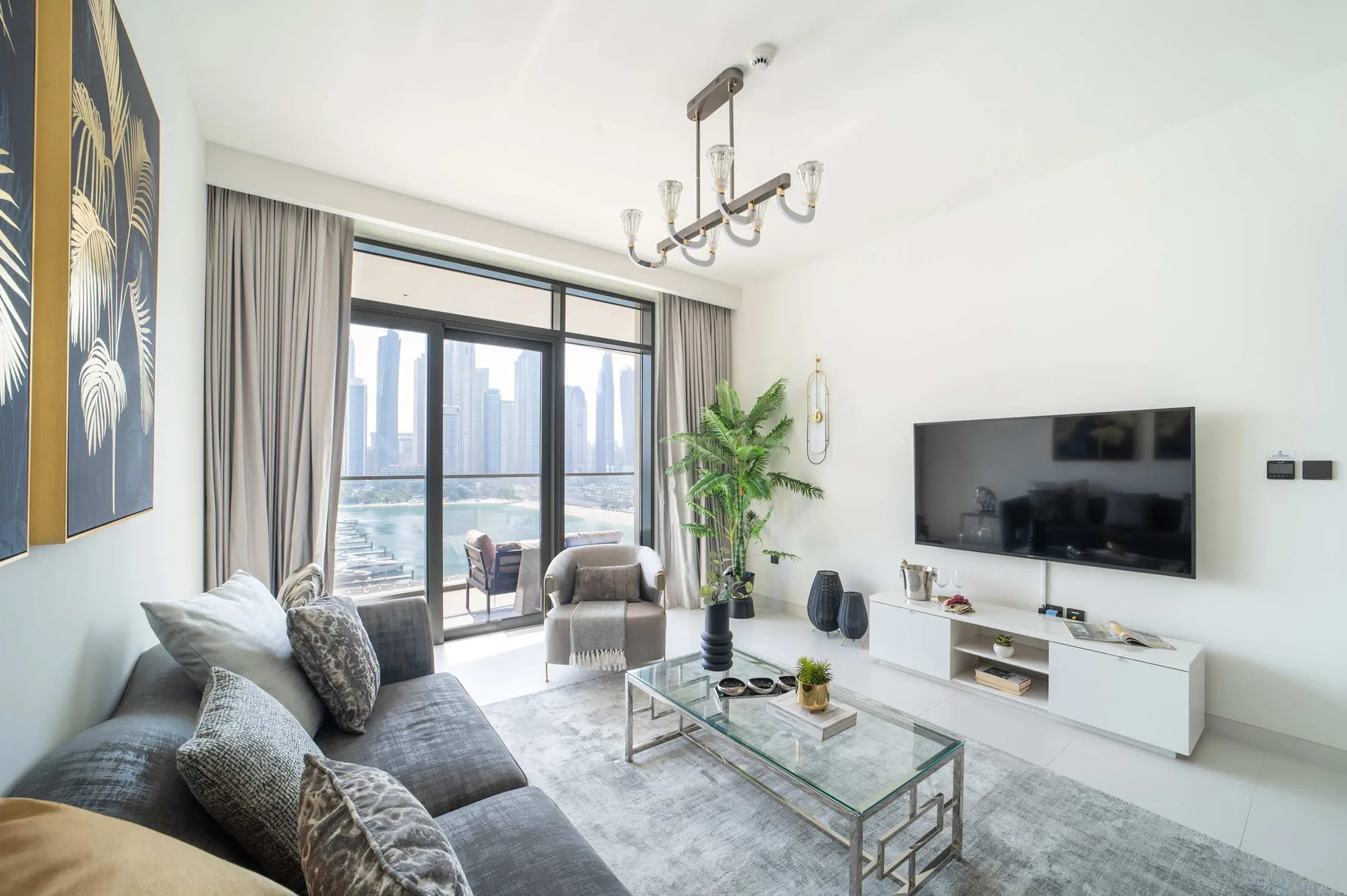 Una sala de estar luminosa con asientos, una mesa de centro de vidrio y un televisor en la pared.