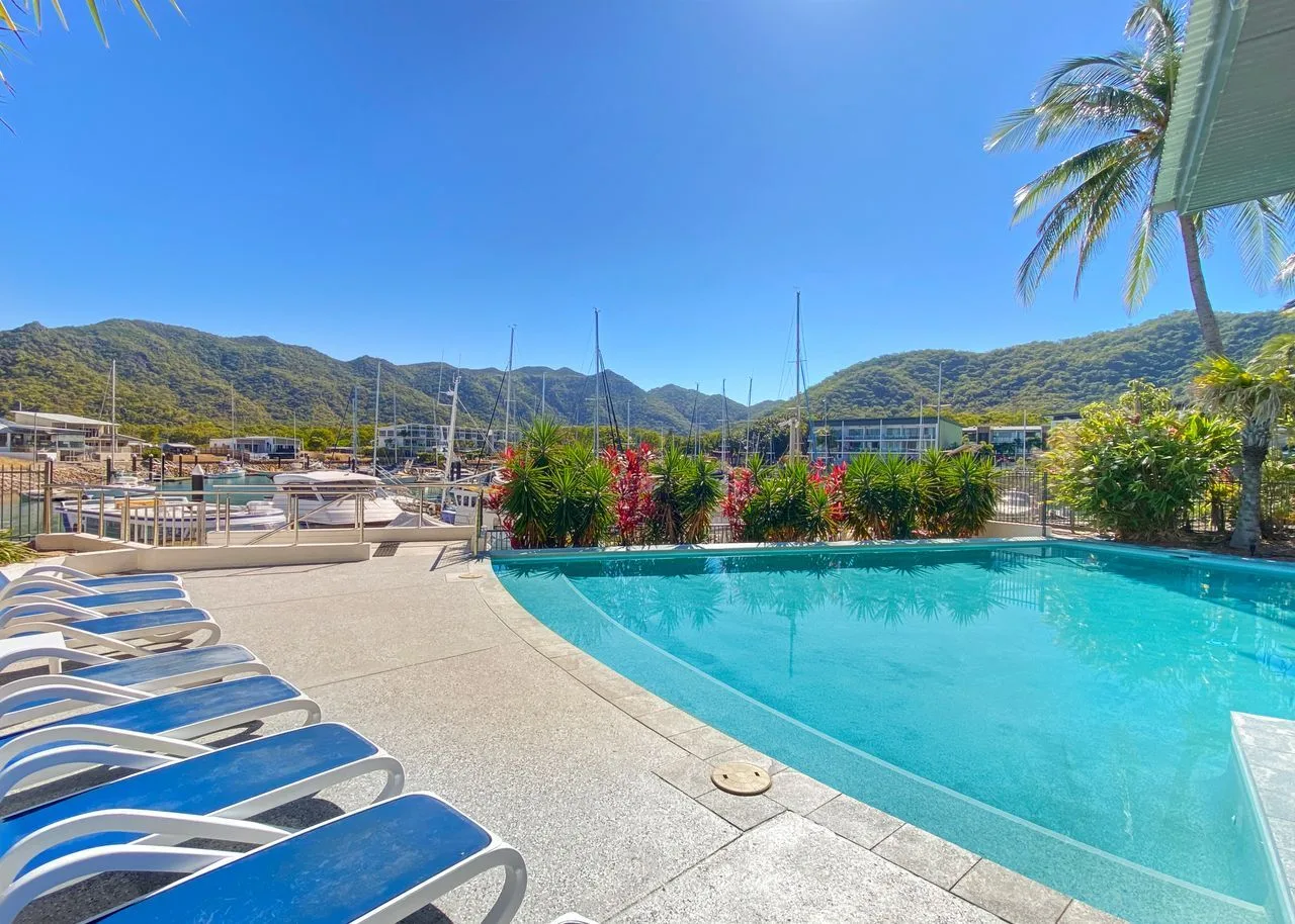 Una piscina junto a asientos para descansar, con palmeras y colinas verdes al fondo.