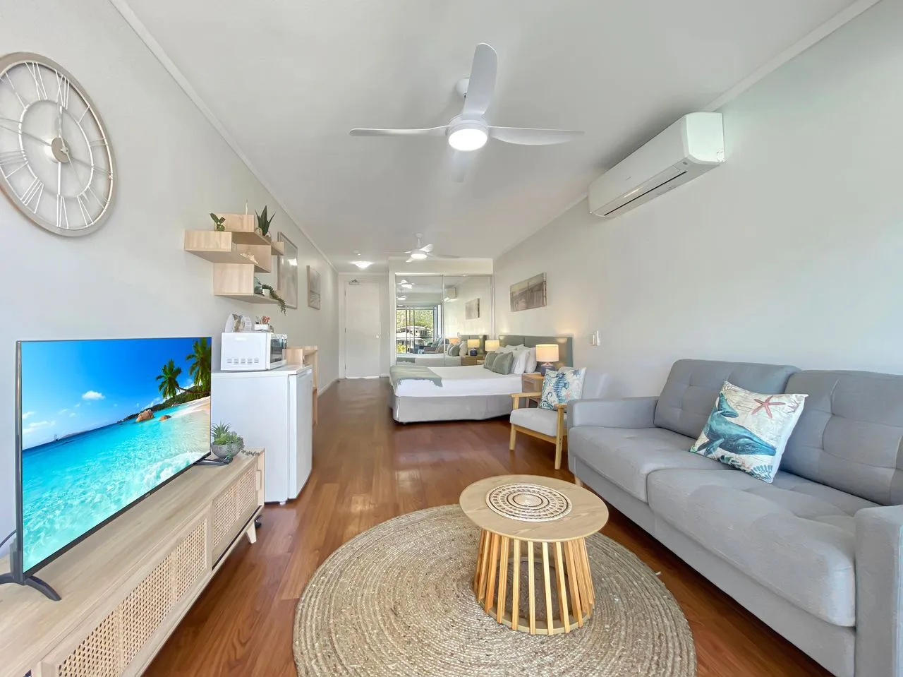 Una habitación tipo estudio luminosa con cama, asientos y televisor.