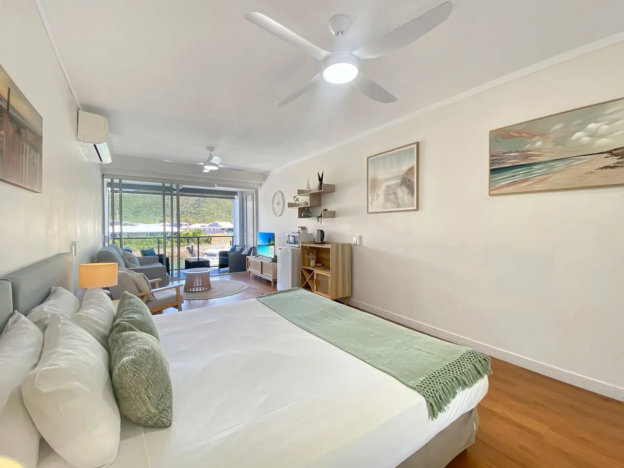 Un estudio luminoso con cama, zona de estar y puertas de vidrio que dan a un balcón.