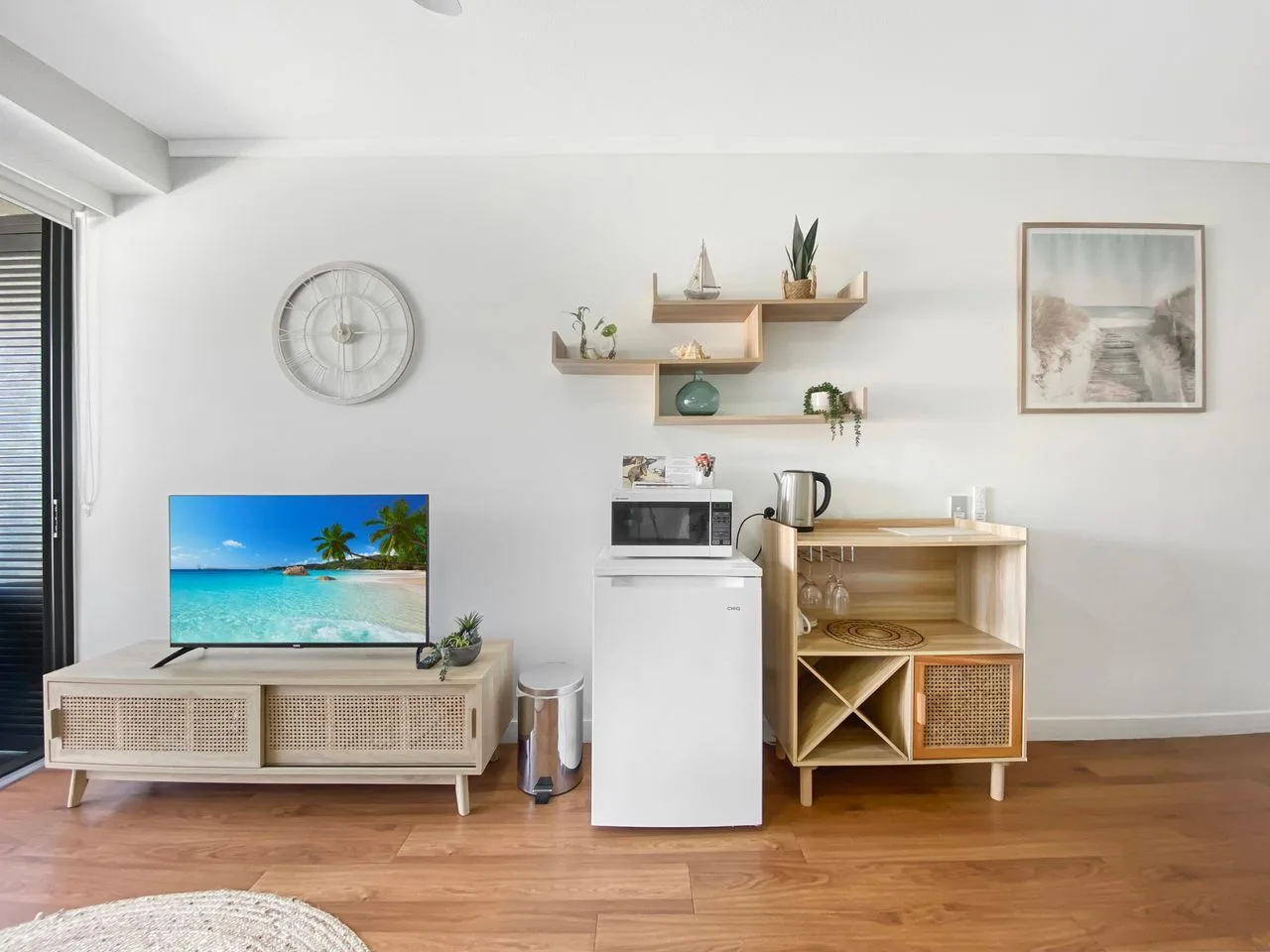 Estudio con televisor, refrigerador compacto y una pequeña cocina de madera.