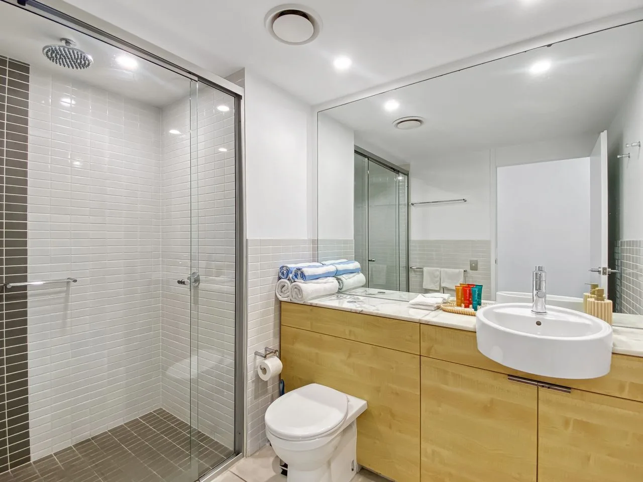 Un baño luminoso con ducha de vidrio, inodoro y un amplio tocador.