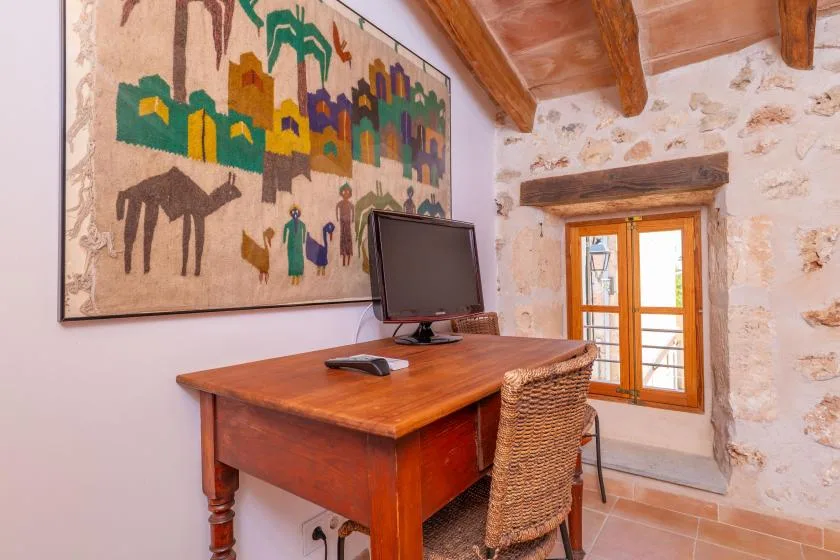 Una habitación rústica con escritorio de madera, monitor y arte colorido en la pared.