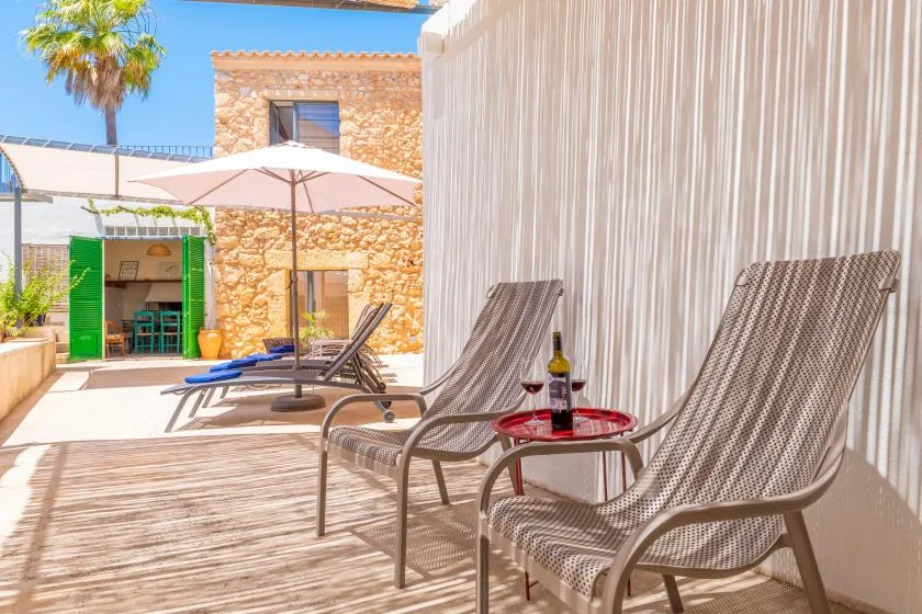Un patio exterior tiene asientos junto a una pequeña mesa roja y una pantalla a rayas.