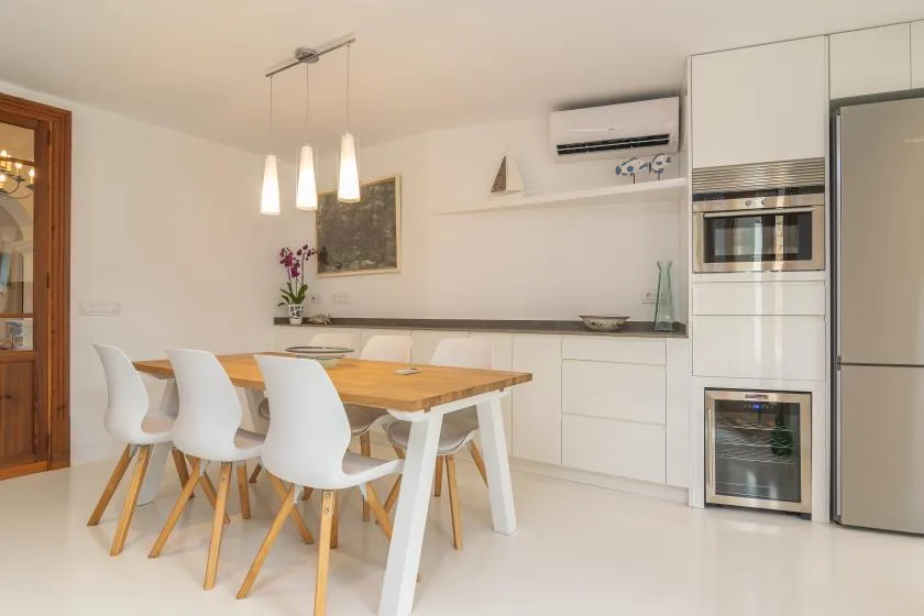 Un comedor luminoso con una mesa de madera junto a una cocina blanca.