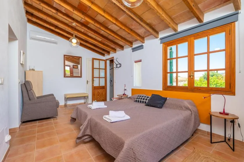 Un dormitorio con una cama, asientos y una gran ventana con marco de madera.
