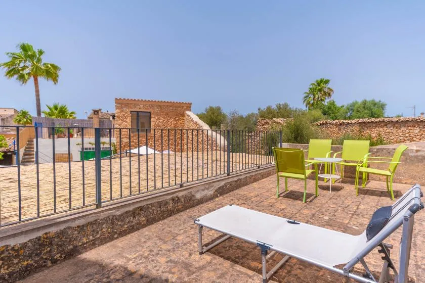 Un patio soleado tiene asientos verde lima y una tumbona junto a una piscina cercada.
