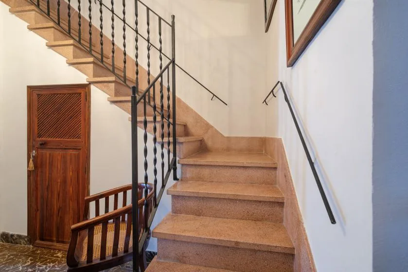Una escalera interior con peldaños de madera y barandillas metálicas oscuras.