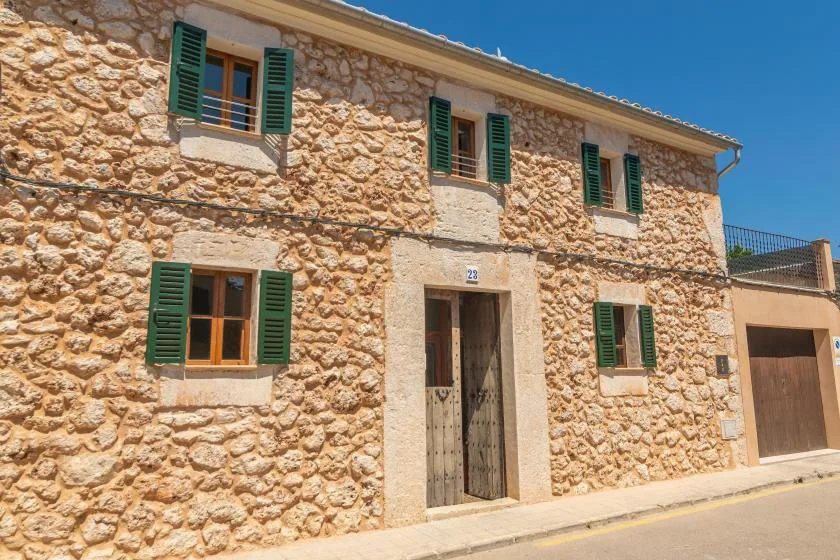 Fachada de una casa de piedra con persianas verdes y una puerta central.