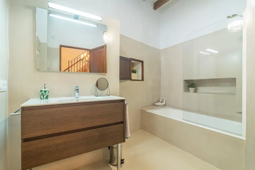 Un baño luminoso con tocador de madera, espejo de pared y bañera.