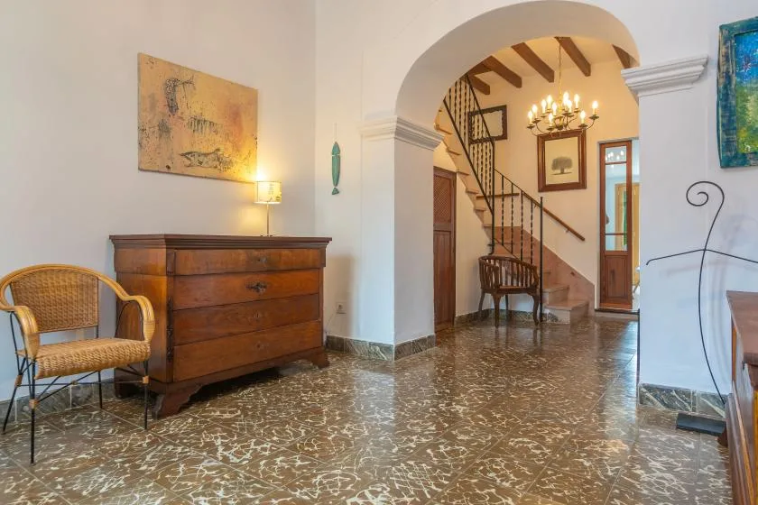 Un pasillo con arco da a una escalera, con un arcón de madera y una silla cerca.