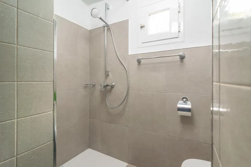 Zona de ducha de baño revestida con azulejos, ducha de mano y accesorios en la pared.