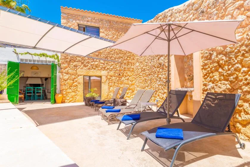 Un patio de piedra soleado tiene asientos reclinables bajo grandes sombrillas.