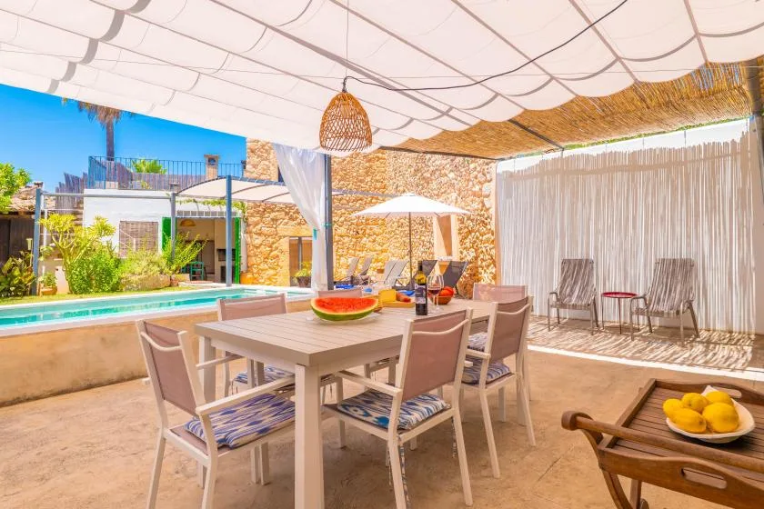 Comedor exterior a la sombra junto a una piscina, con mesa y sillas.