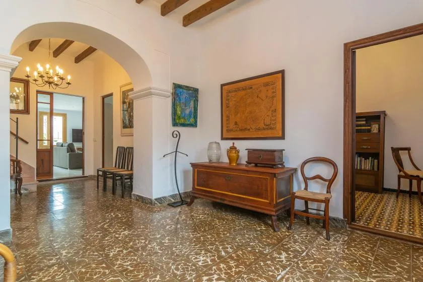 Un pasillo interior con un arco, un mueble de madera y cuadros enmarcados.