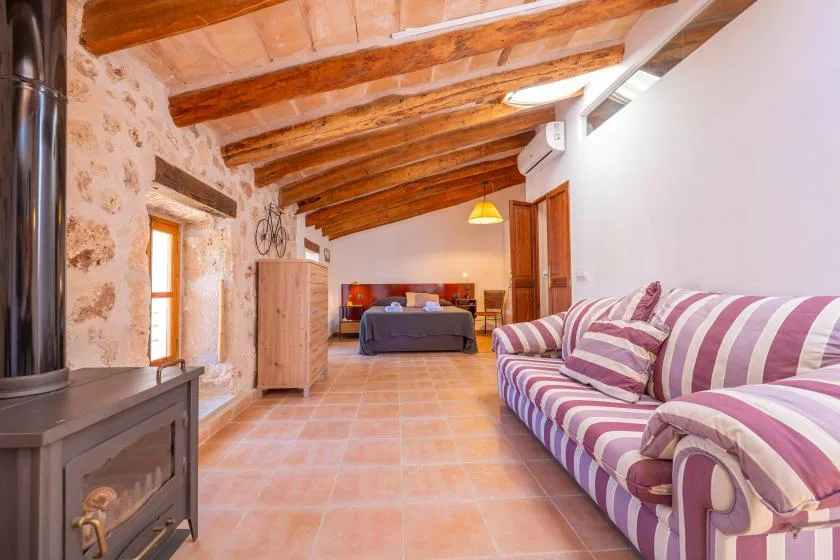 Un salón rústico con asientos a rayas, vigas de madera vistas y una cama al fondo.