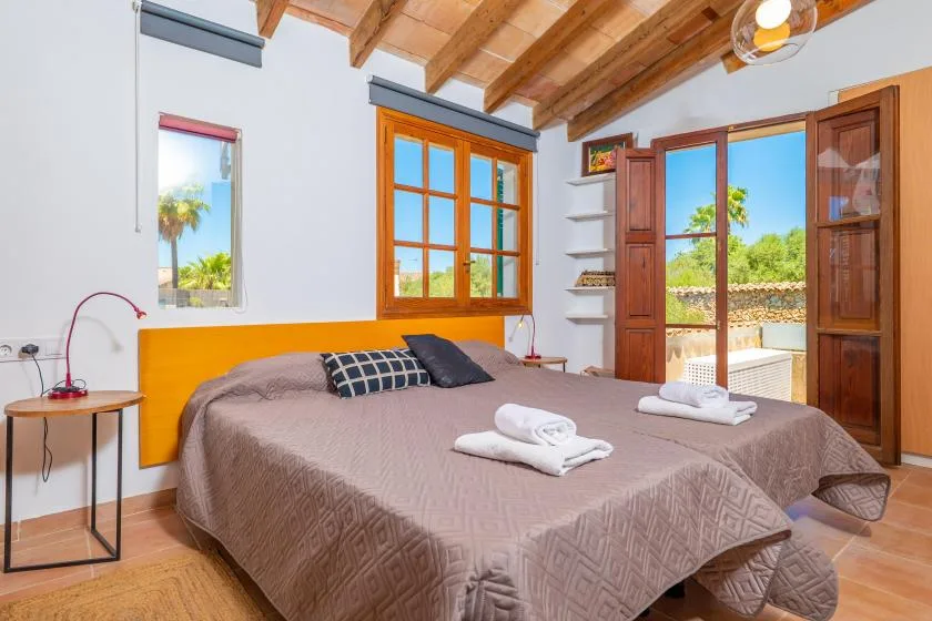 Un dormitorio con una cama grande, vigas de madera en el techo y puertas abiertas al balcón.