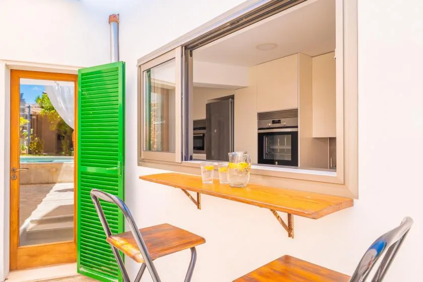 Una pequeña zona de comedor exterior con una barra en la pared y una ventana abierta a la cocina.