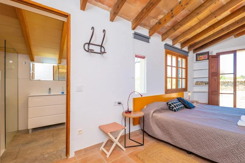 Un dormitorio con una cama grande, vigas de madera a la vista y un baño contiguo.