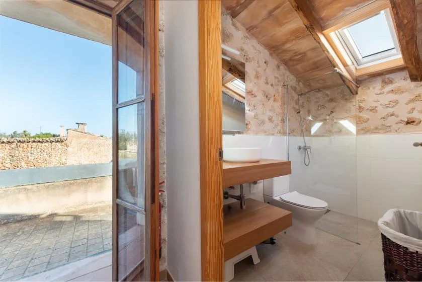 Un baño con mueble de madera, techo inclinado y tragaluz.